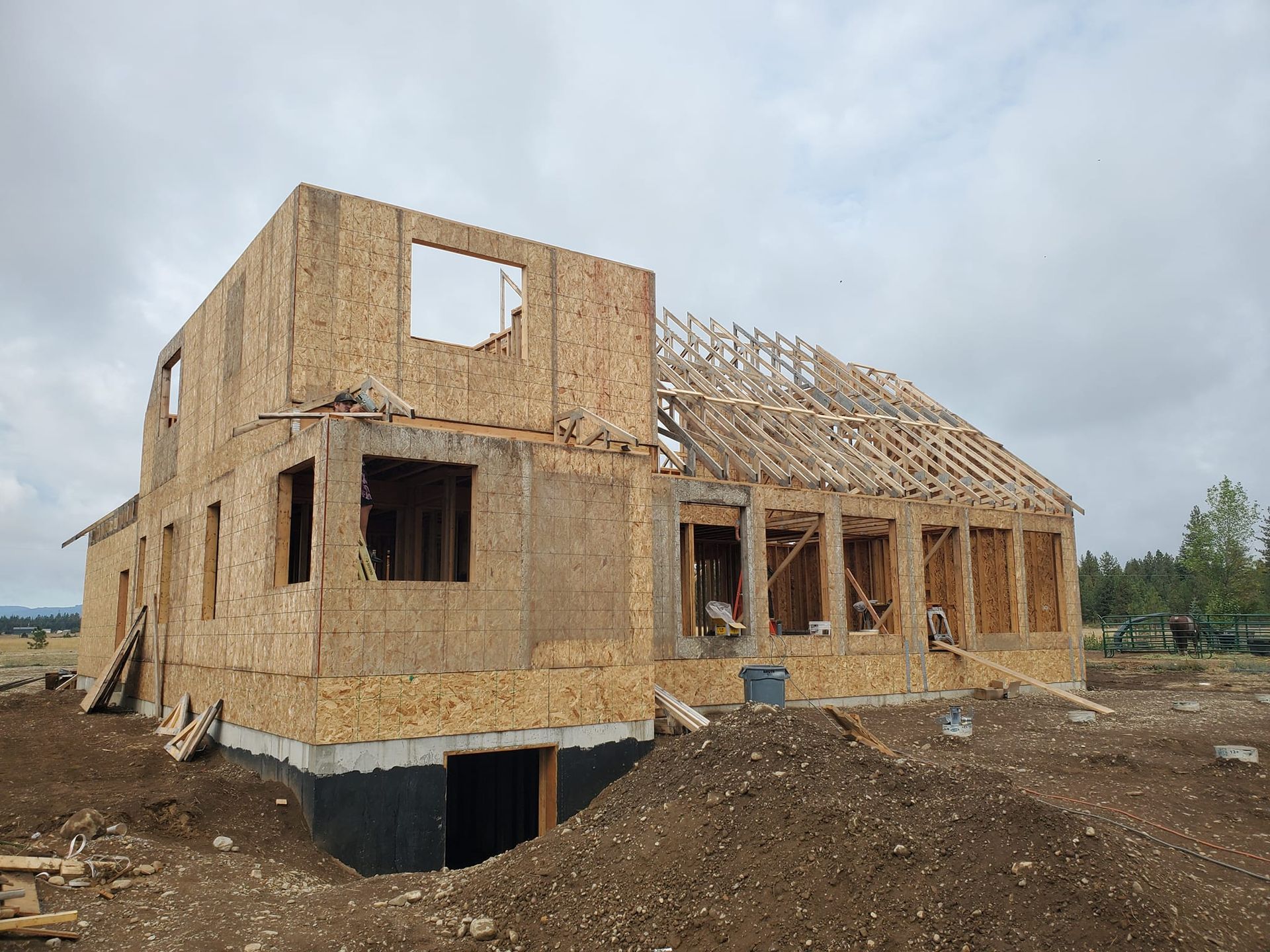 Partially built plywood house framing on a dirt lot under a cloudy sky