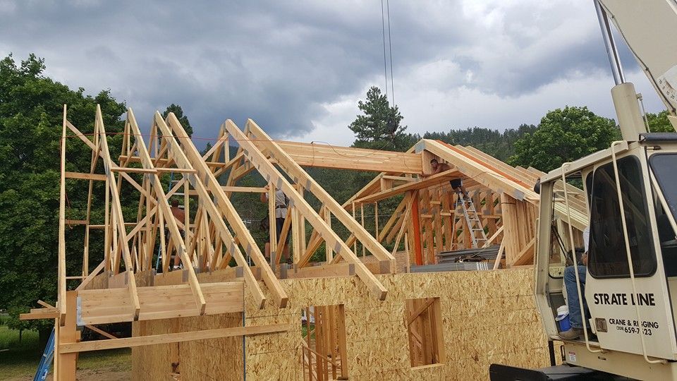 Wooden house frame under construction with roof trusses and a white truck beside it.