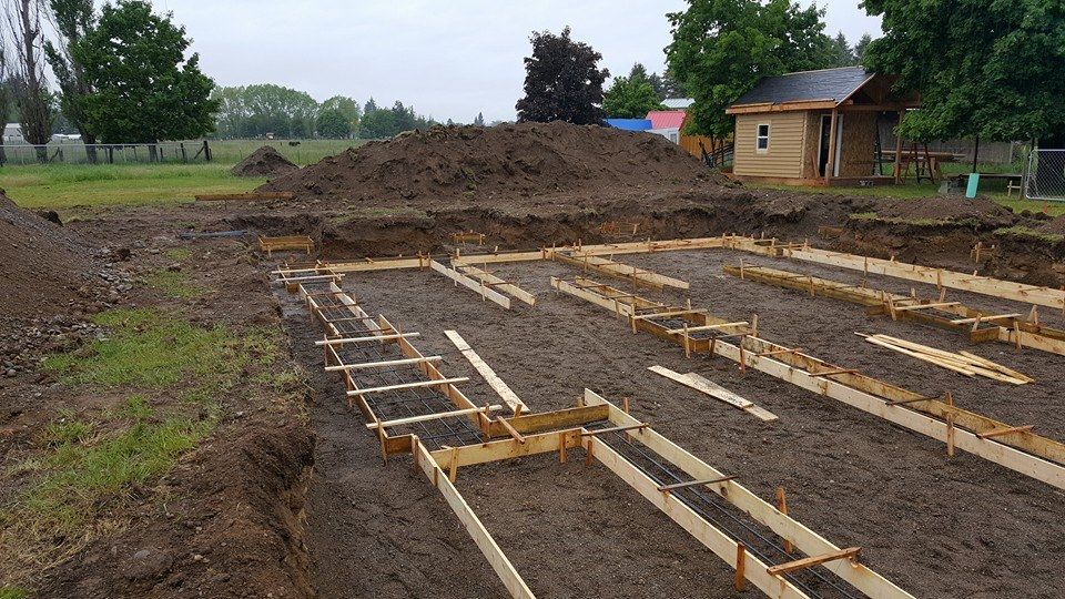 Wooden foundation forms laid out on a dirt construction site beside a small house and soil piles.