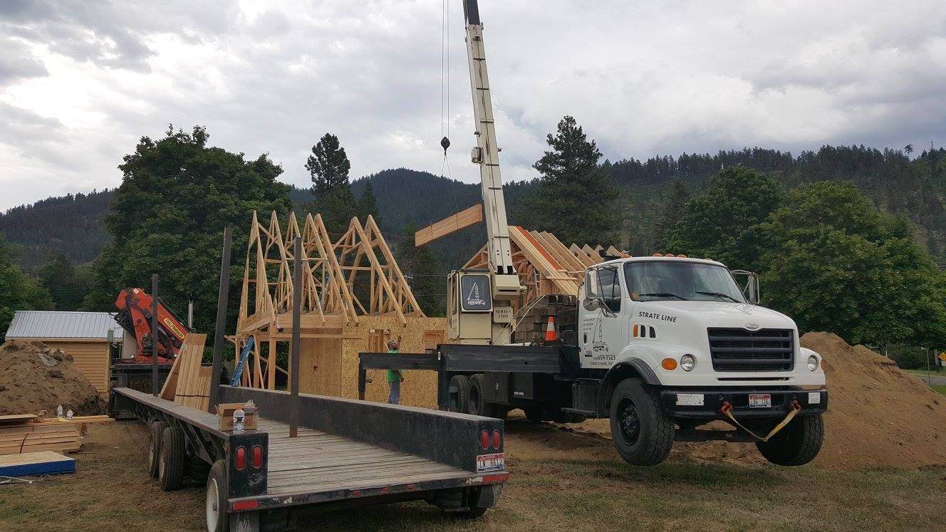 Construction site with a crane truck and wooden house framing on a dirt lot