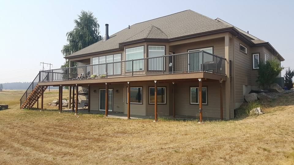 Two-story brown house with a raised deck and stairs on a dry grassy lot