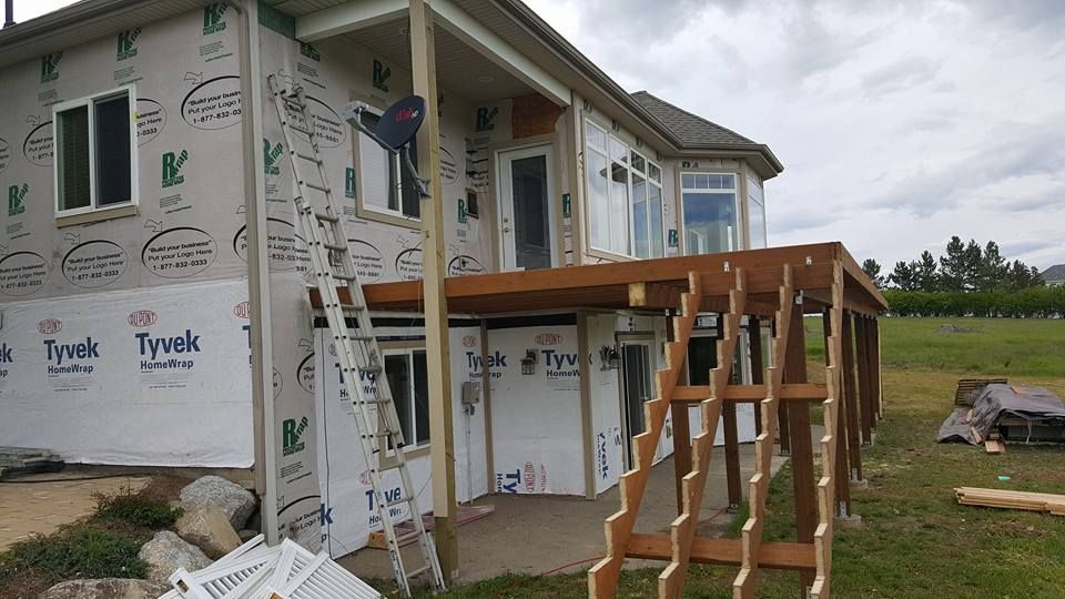 Partially built house with Tyvek wrap and a wooden deck frame under construction on a cloudy day