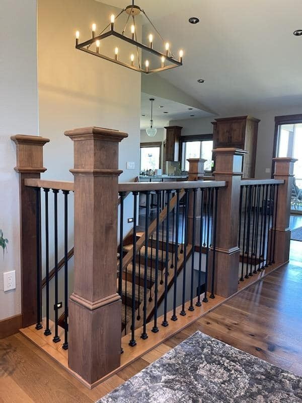 Stair railing with black balusters and wood posts in a bright home interior near a chandelier