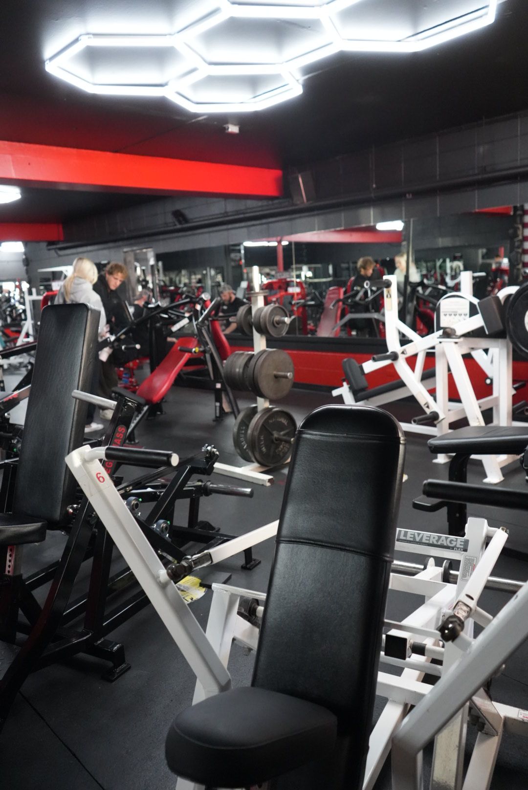 Modern gym interior with black and red equipment and bright hexagonal ceiling lights