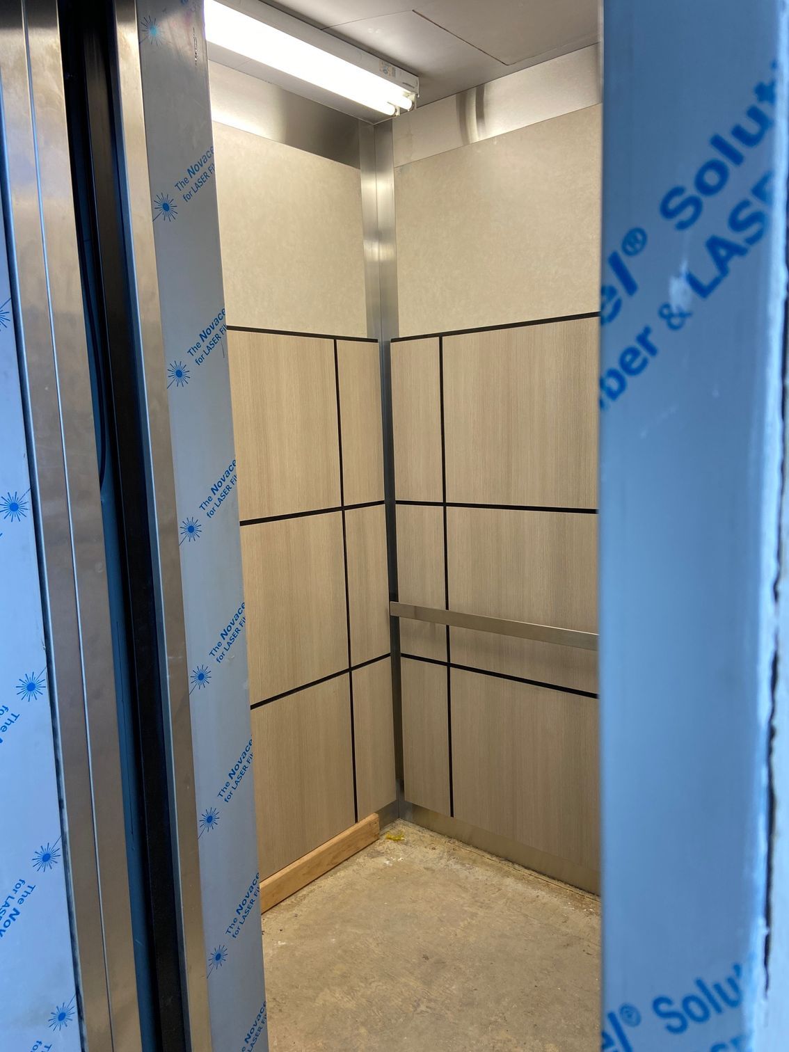Interior of an elevator with light wood paneling, metal trim, and exposed metal frame.