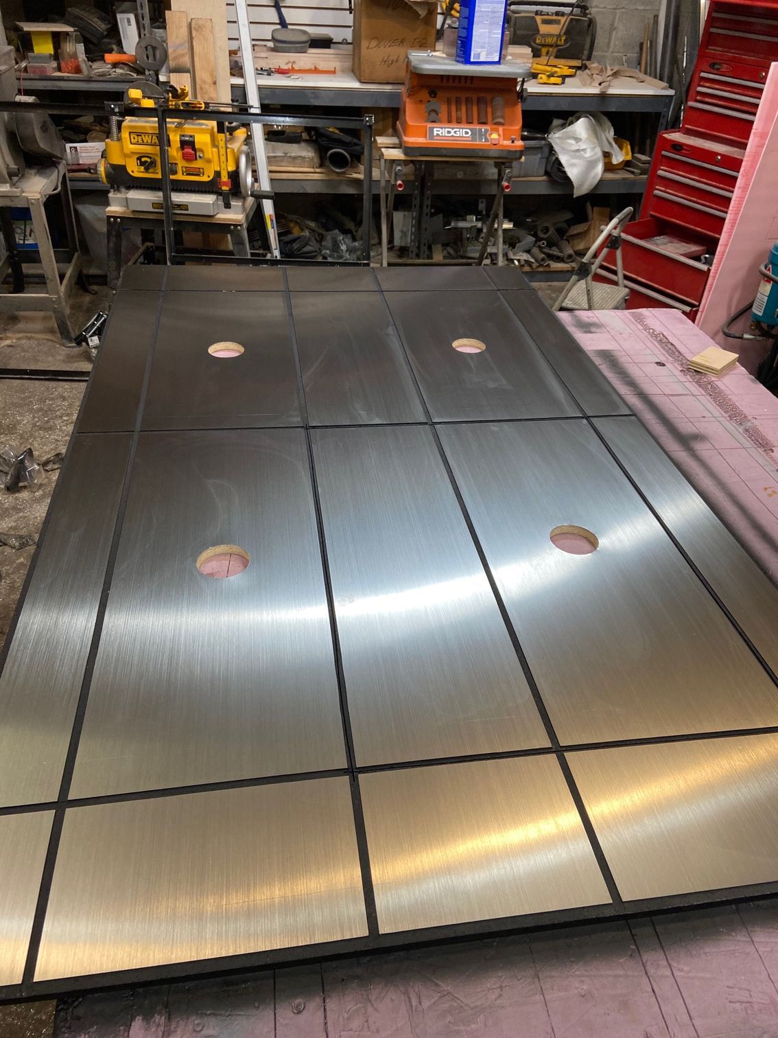 Large, metal table in a workshop, divided into sections with circular holes.