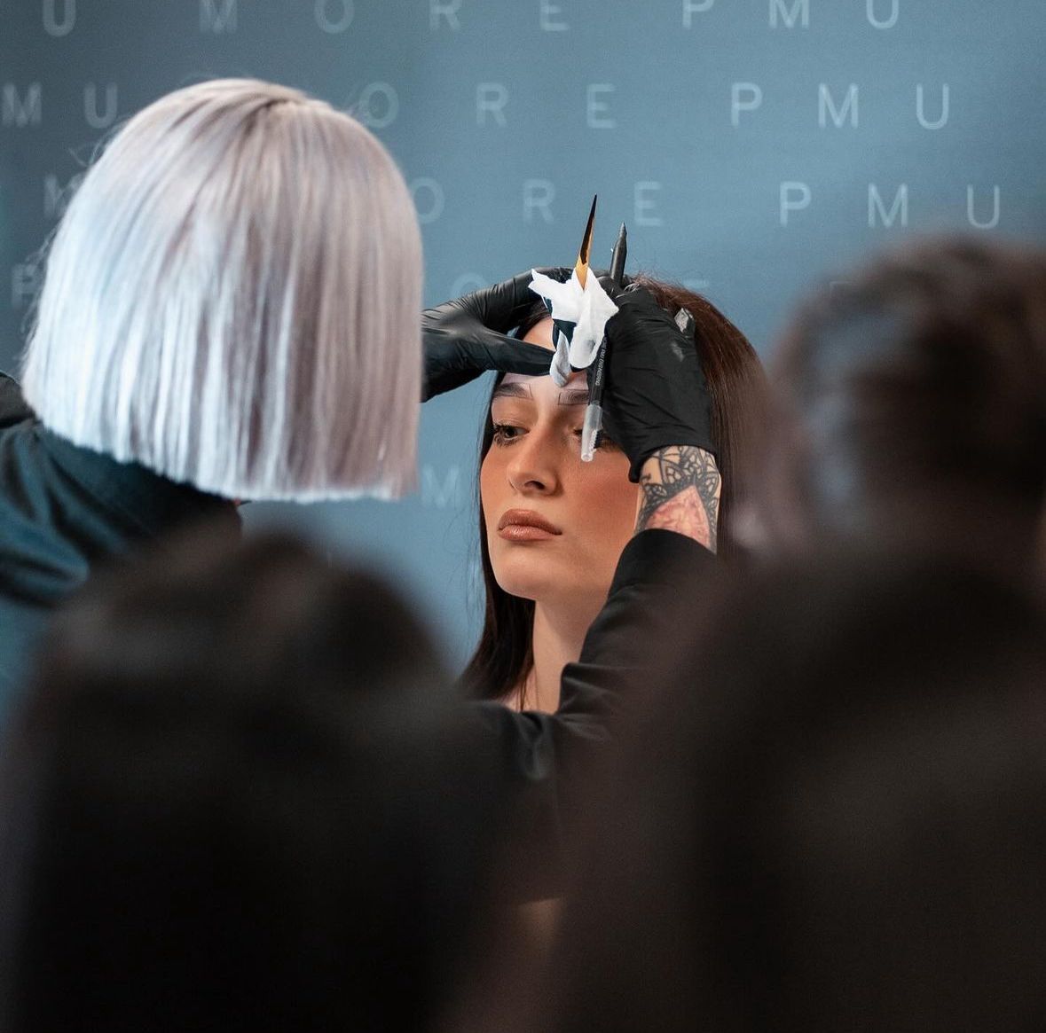 Un tatuatore applica uno stencil a forma di stella sulla fronte di un cliente durante un evento affollato.