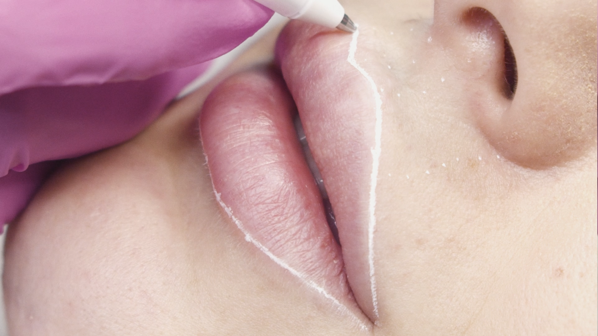 Primo piano delle labbra mentre si applica il rossetto rosa con un pennello.