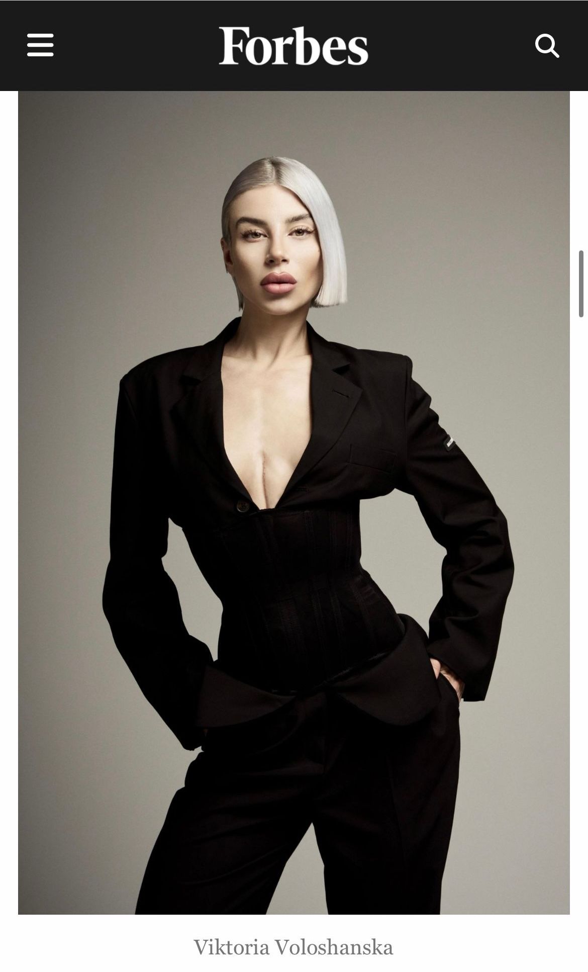Pagina di Forbes che mostra un modello in abito nero con profonda scollatura a V su sfondo grigio