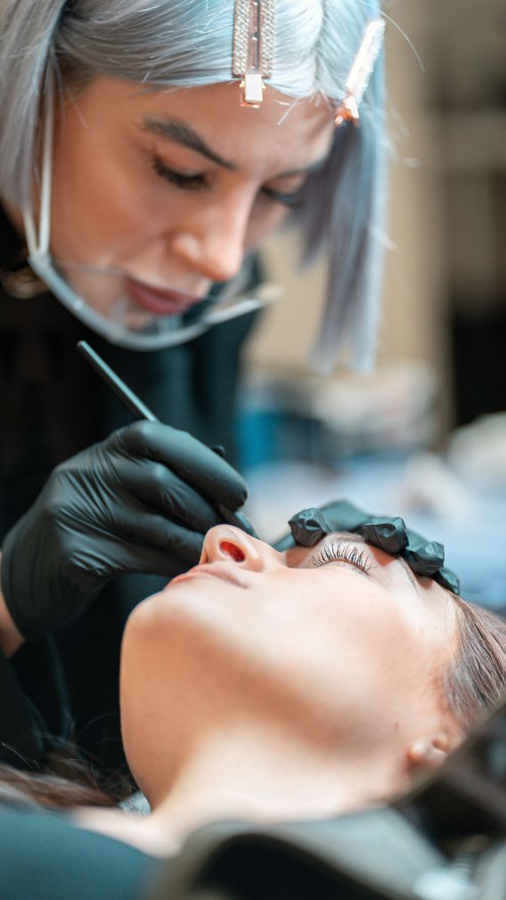 Persona che applica il trucco sull'occhio chiuso di una cliente con un pennello e guanti neri in uno studio.