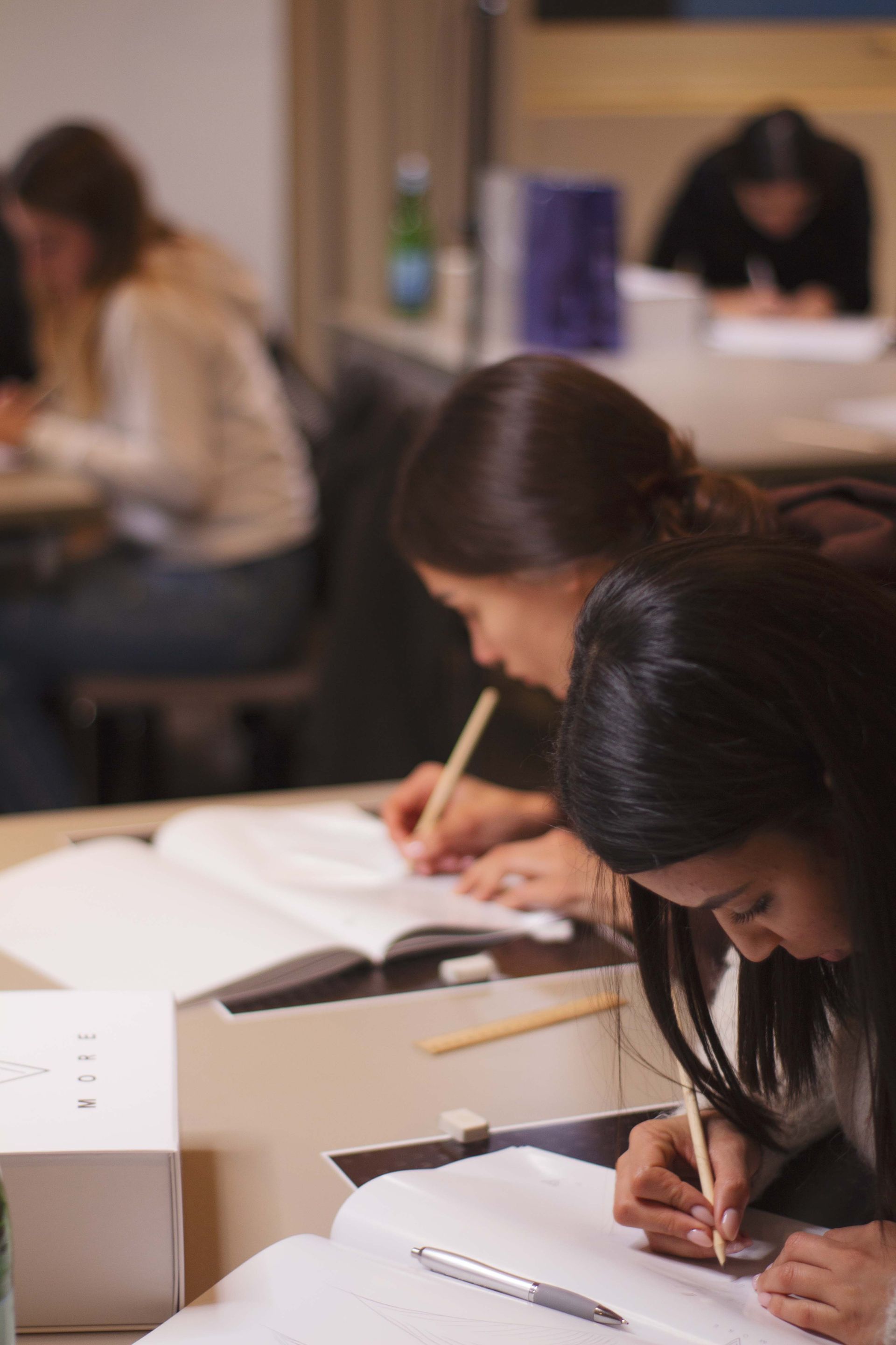 Studenti che scrivono ai banchi in un'aula, con fogli e quaderni sparsi ovunque.