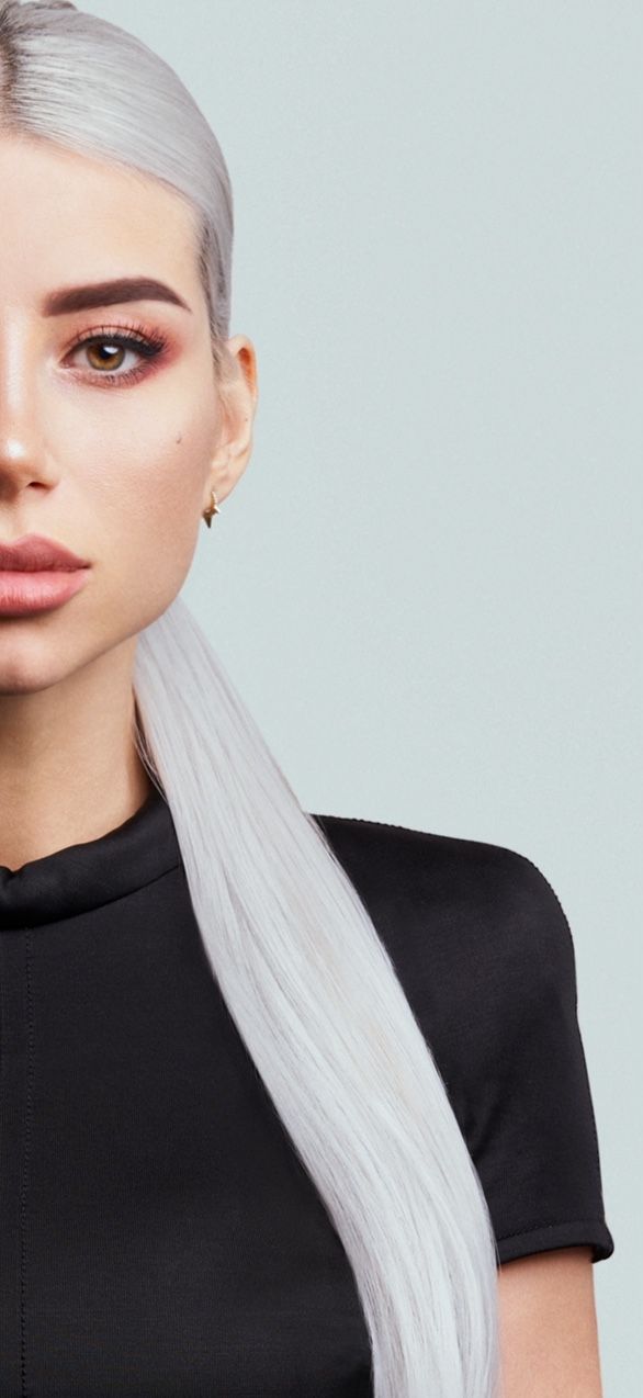 Primo piano di una persona con i capelli biondo platino che indossa una maglietta nera su uno sfondo grigio chiaro.