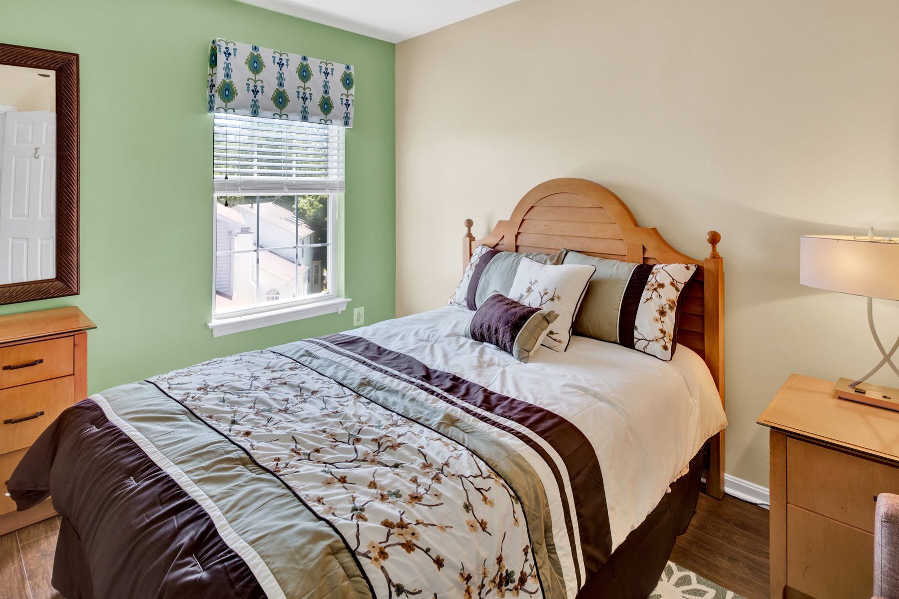 A bedroom with a bed , nightstand , mirror and window.
