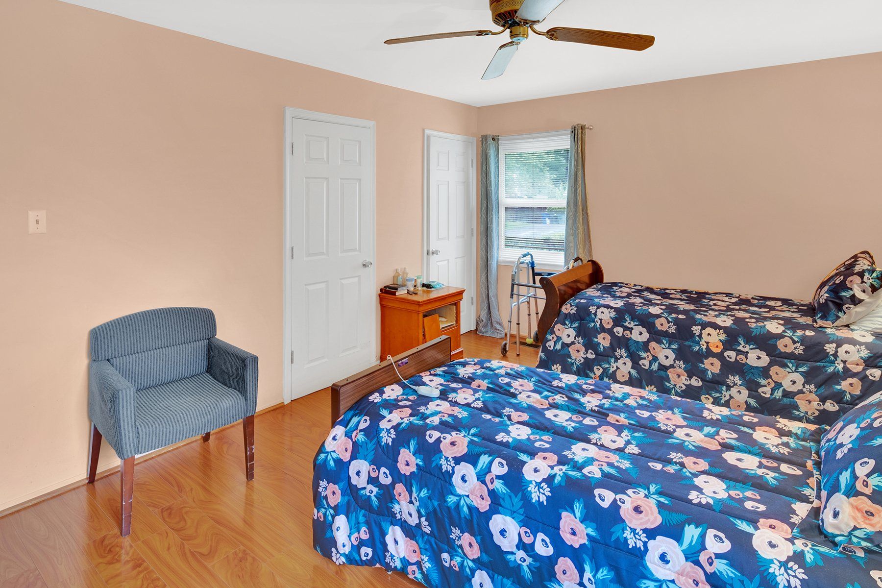 A bedroom with two beds , a chair and a ceiling fan.