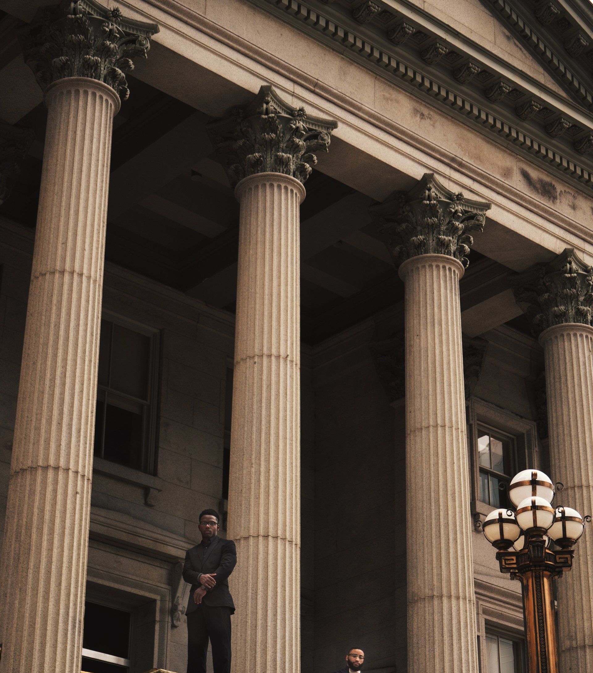 A man in a suit stands in front of a building with columns