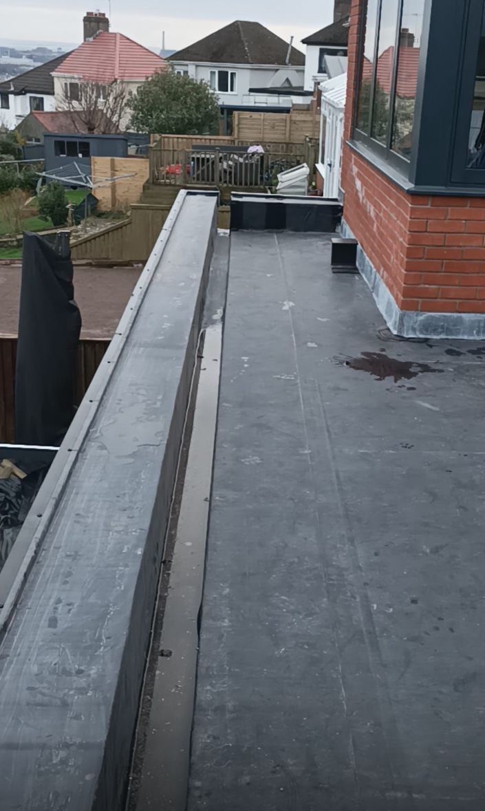 A roof with a drain on it and a brick building in the background.