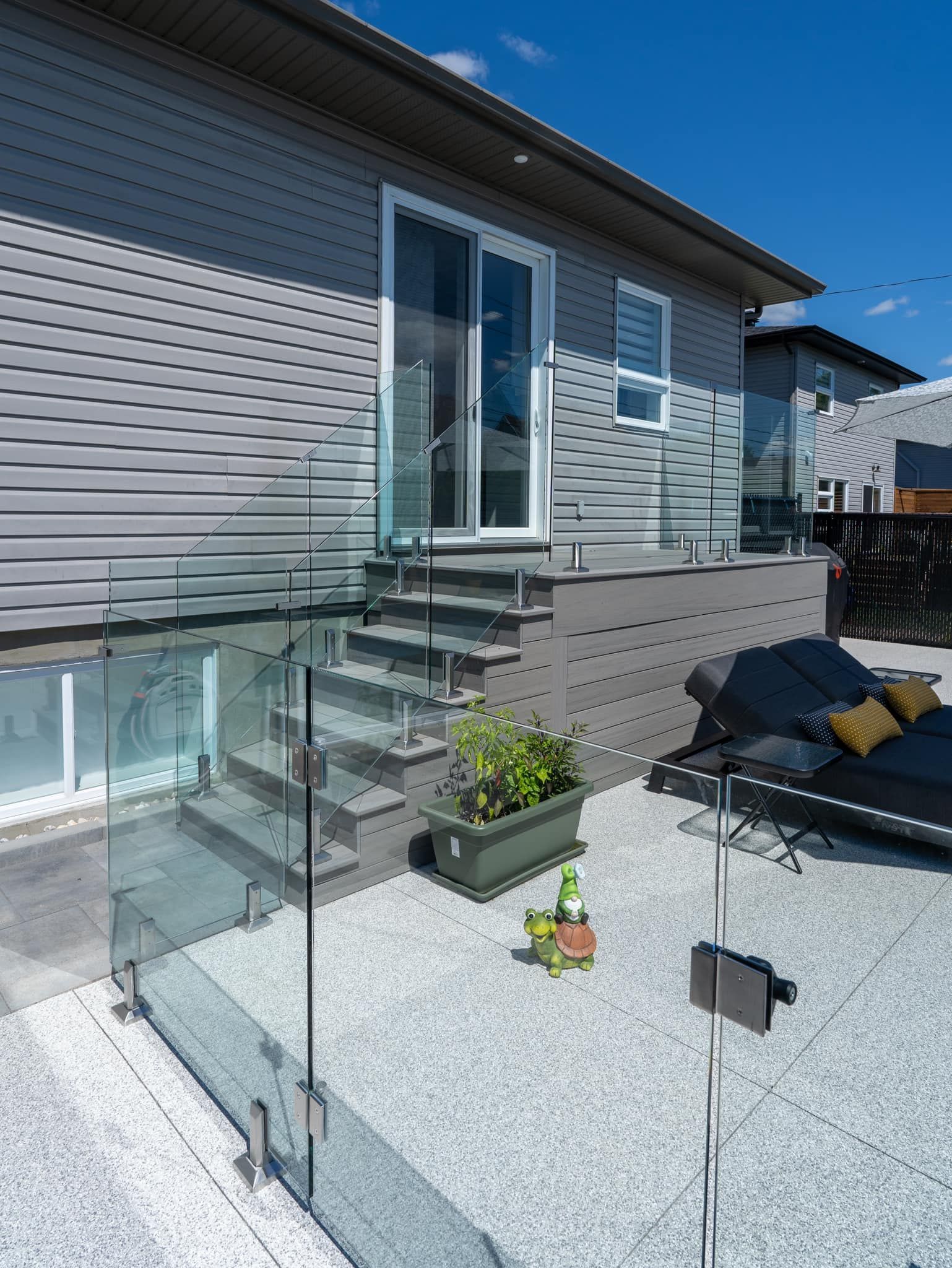 Terrasse extérieure avec balustrade en verre, marches et porte coulissante donnant sur un bâtiment aux murs gris.
