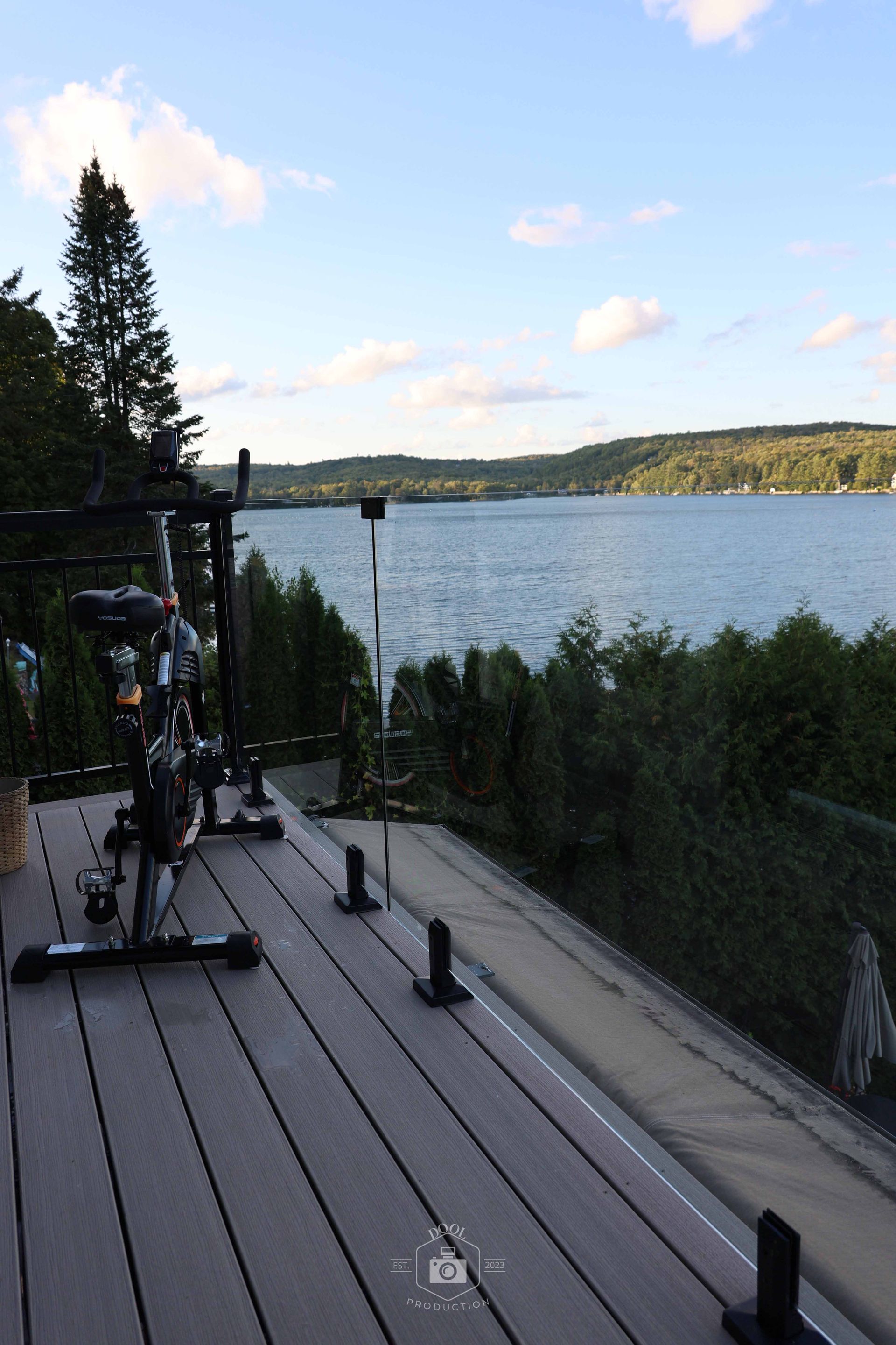 Vélo d'appartement sur une terrasse surplombant un lac, avec des arbres et un ciel bleu.