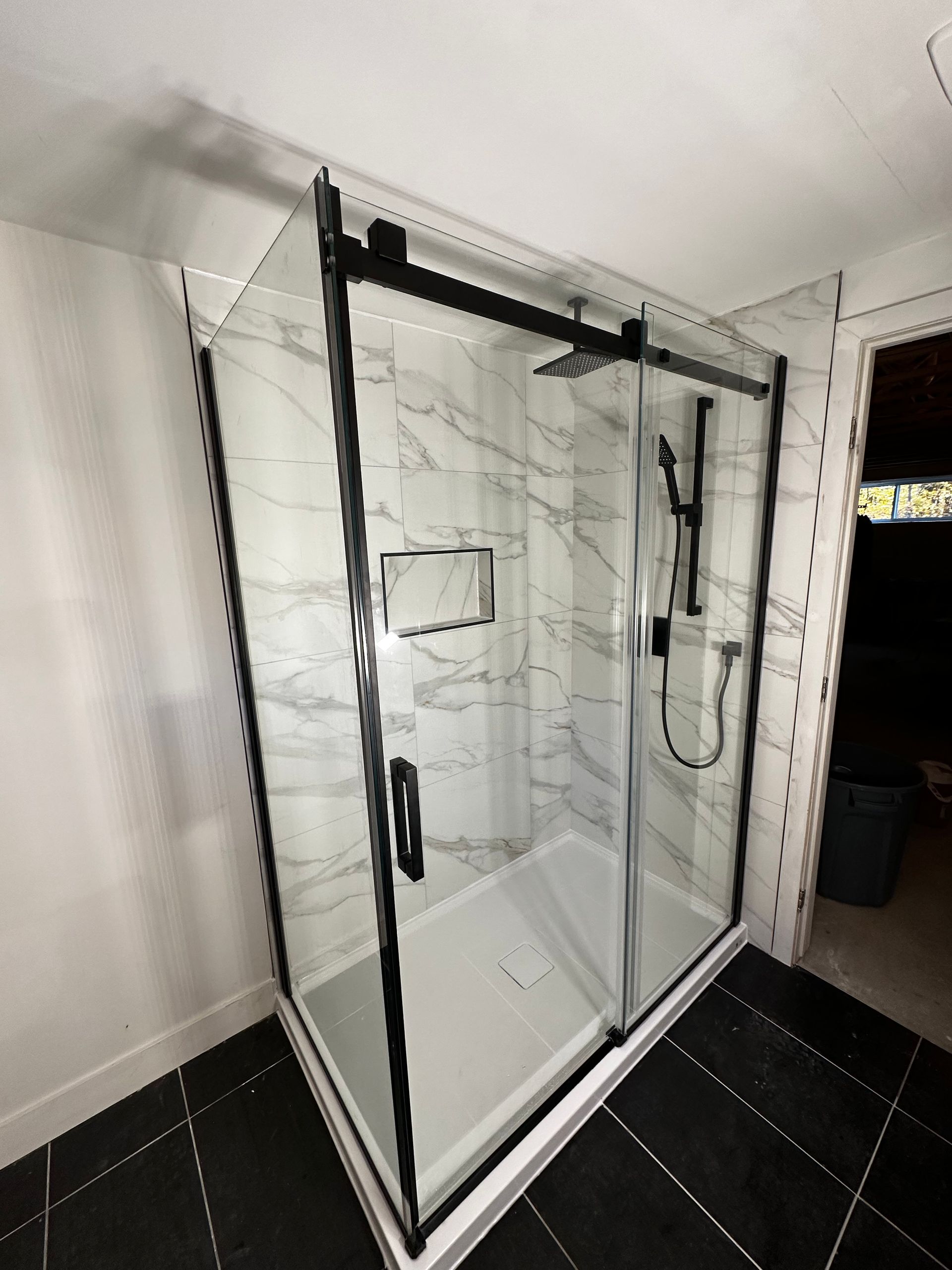 Cabine de douche moderne avec finitions noires, parois imitation marbre et portes coulissantes en verre dans une salle de bains.