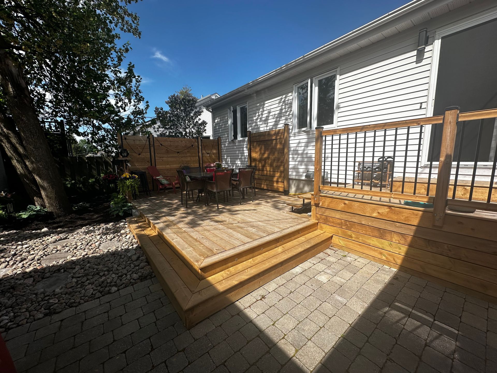 Terrasse et patio en bois avec mobilier de jardin, attenants à une maison par une journée ensoleillée.