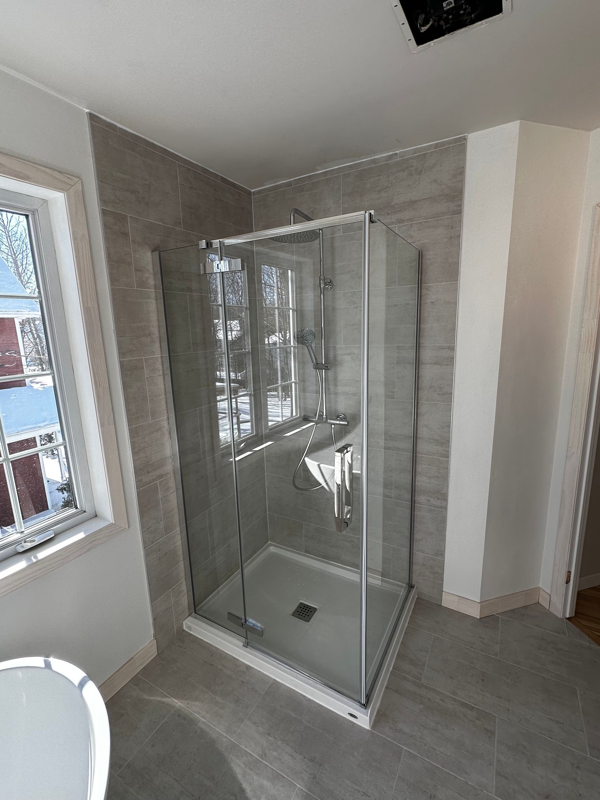 Cabine de douche moderne avec portes en verre, adossée à des murs carrelés et une fenêtre.