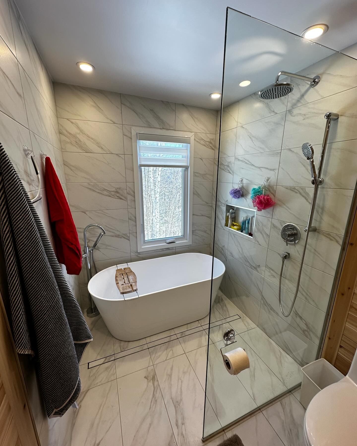 Salle de bains moderne avec baignoire îlot blanche, douche et murs et sol carrelés imitation marbre.