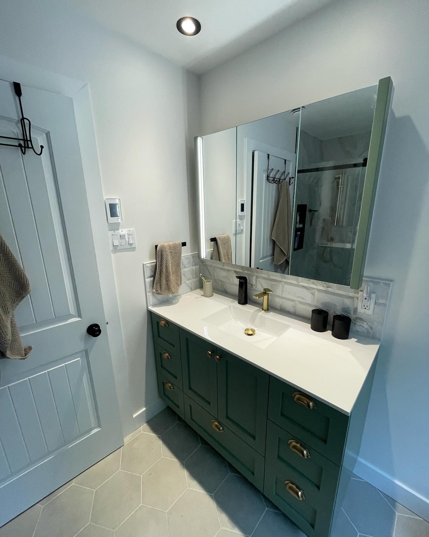 Meuble-lavabo vert pour salle de bain avec miroir, comptoir blanc et accents dorés.