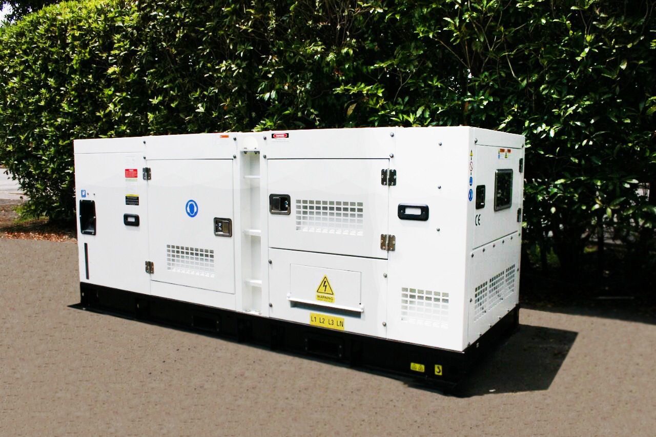 Caja de generador industrial blanca sobre una superficie pavimentada, con un fondo de follaje verde como telón de fondo.