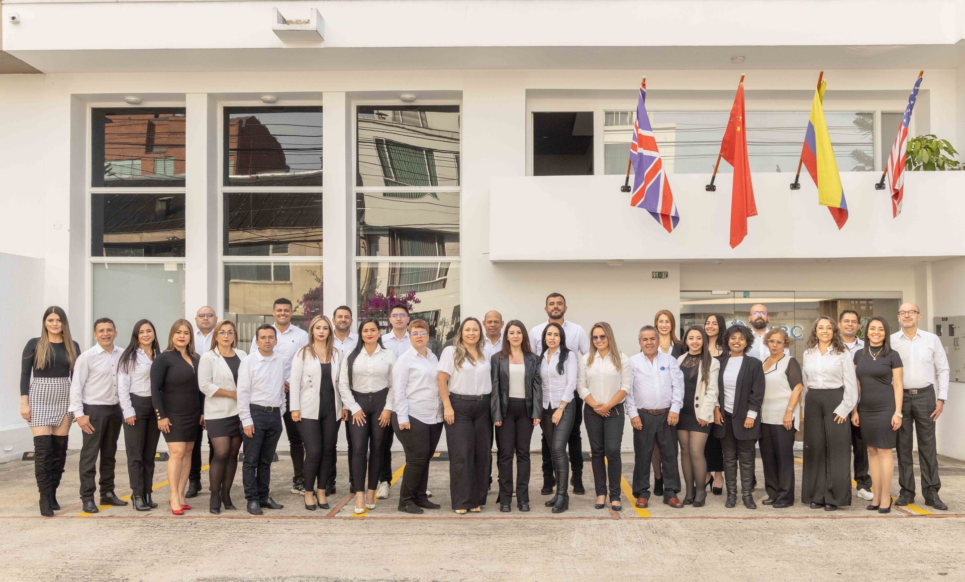 Grupo de personas vestidas de negocios posando afuera de un edificio con banderas de diferentes países.