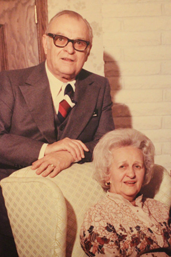 A man in a suit and tie sits next to a woman in a chair