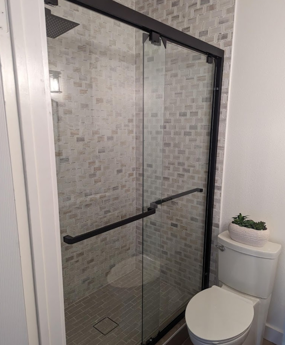 A bathroom with a toilet , shower and glass door.