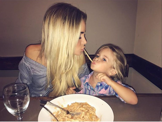 Two people sharing spaghetti at a restaurant table, leaning in close and looking at each other.