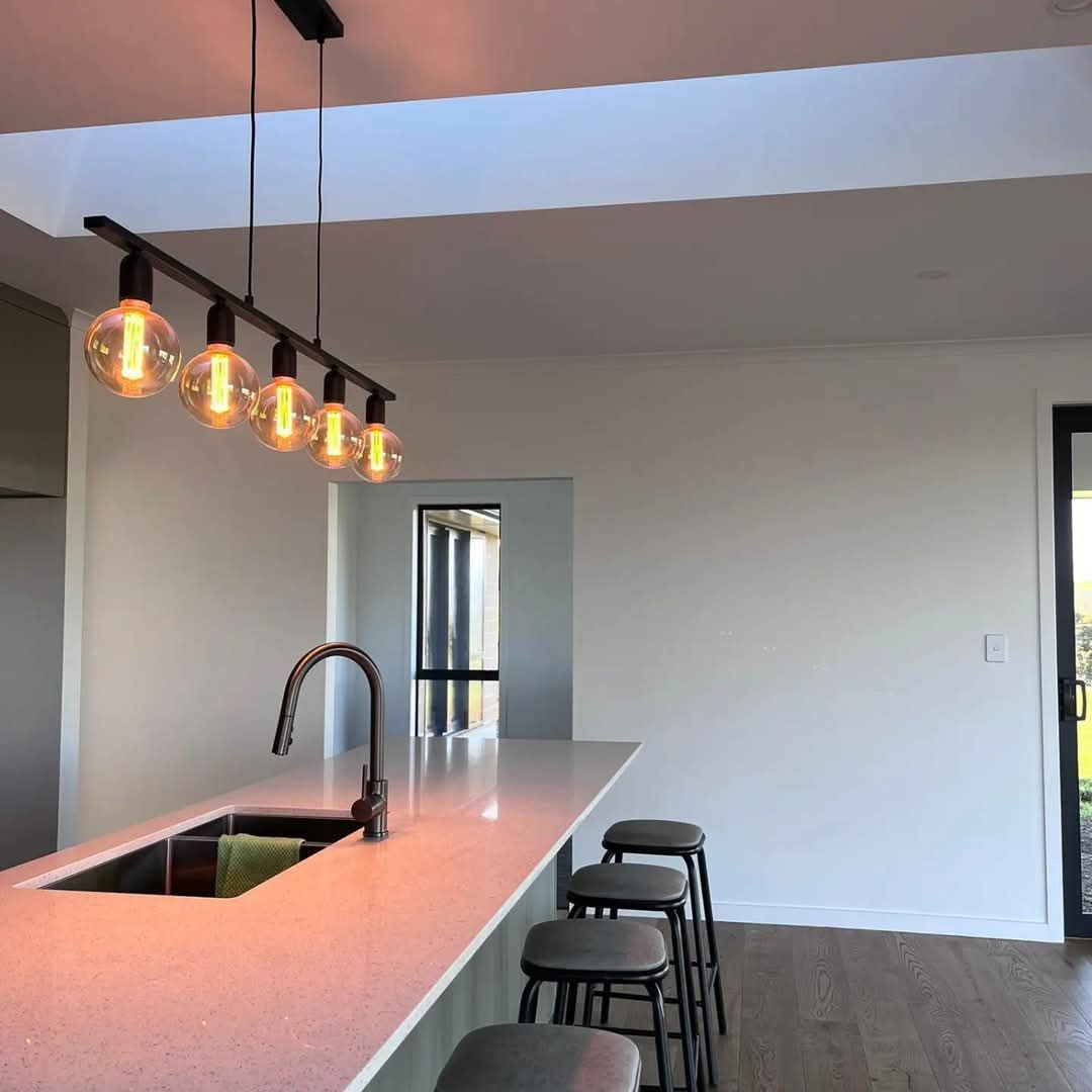 A kitchen with a sink , stools and lights hanging from the ceiling.