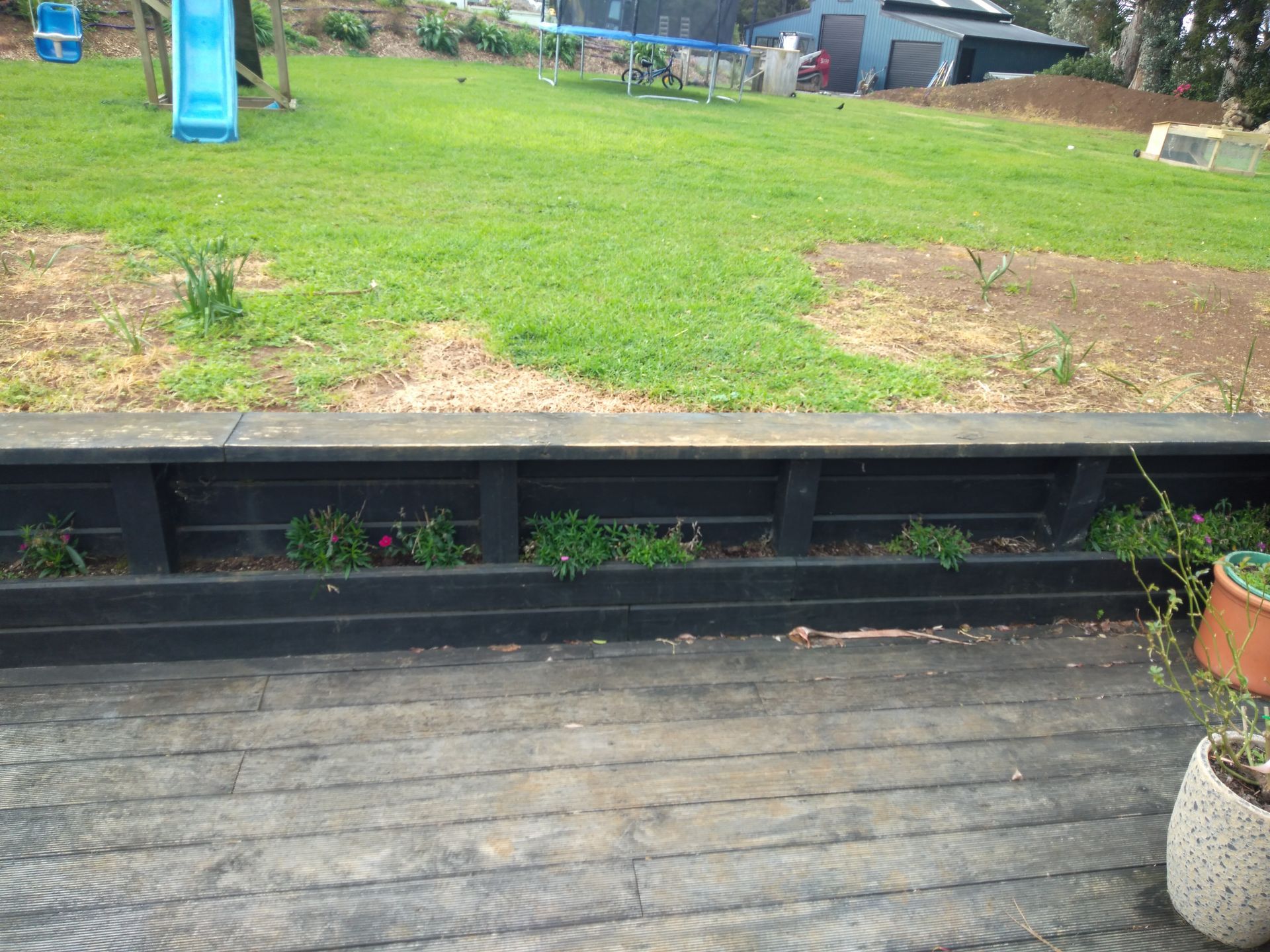 A wooden deck with potted plants and a slide in the background