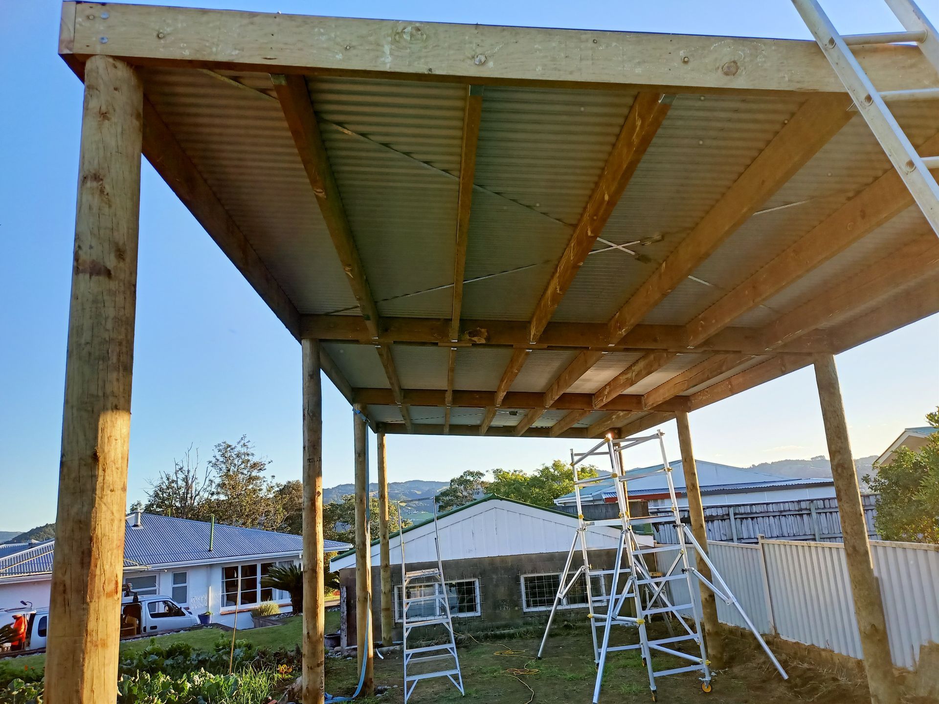 A wooden structure with a metal roof is being built in a backyard.