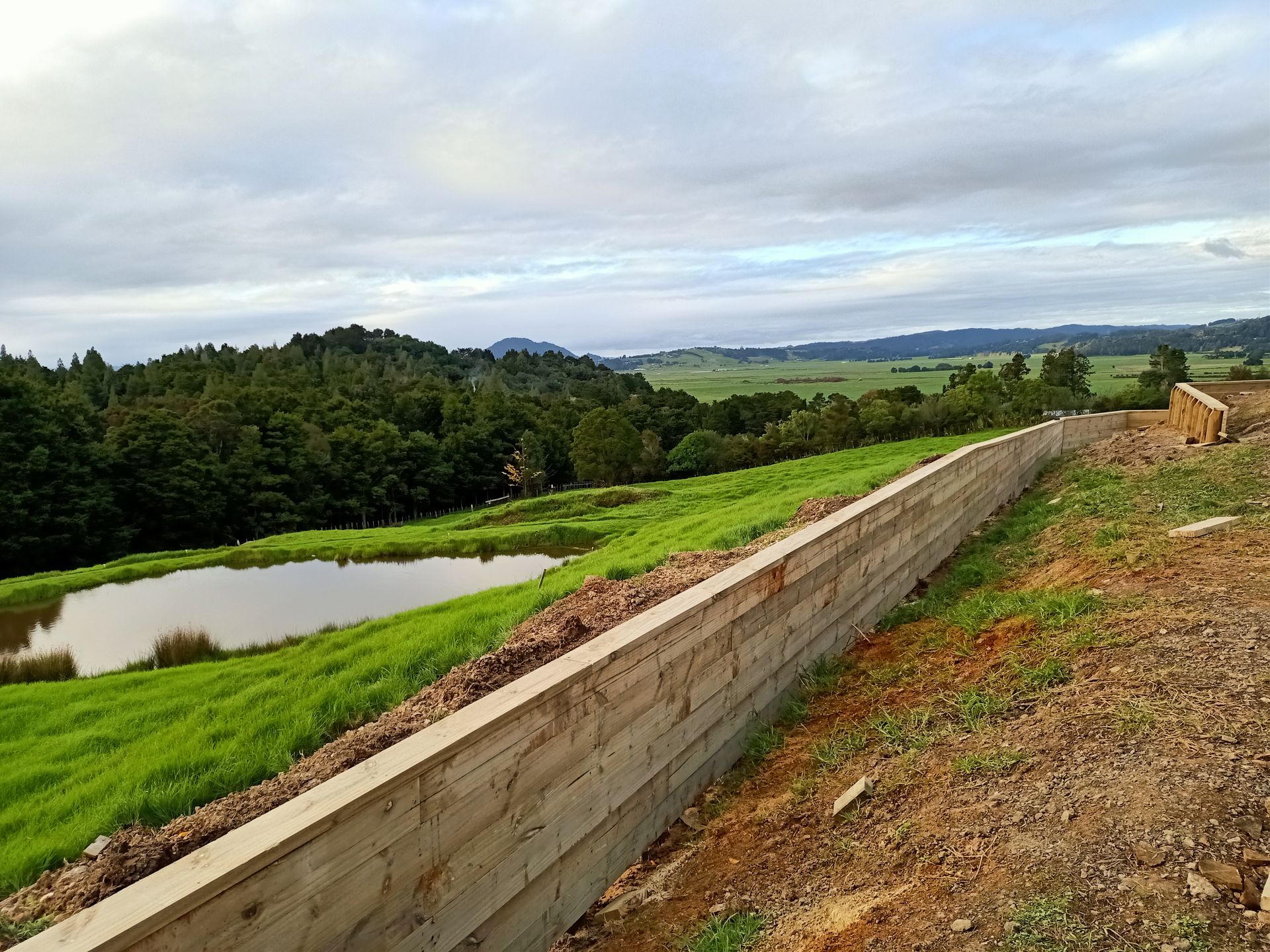 A wooden fence surrounds a small pond in the middle of a grassy field.