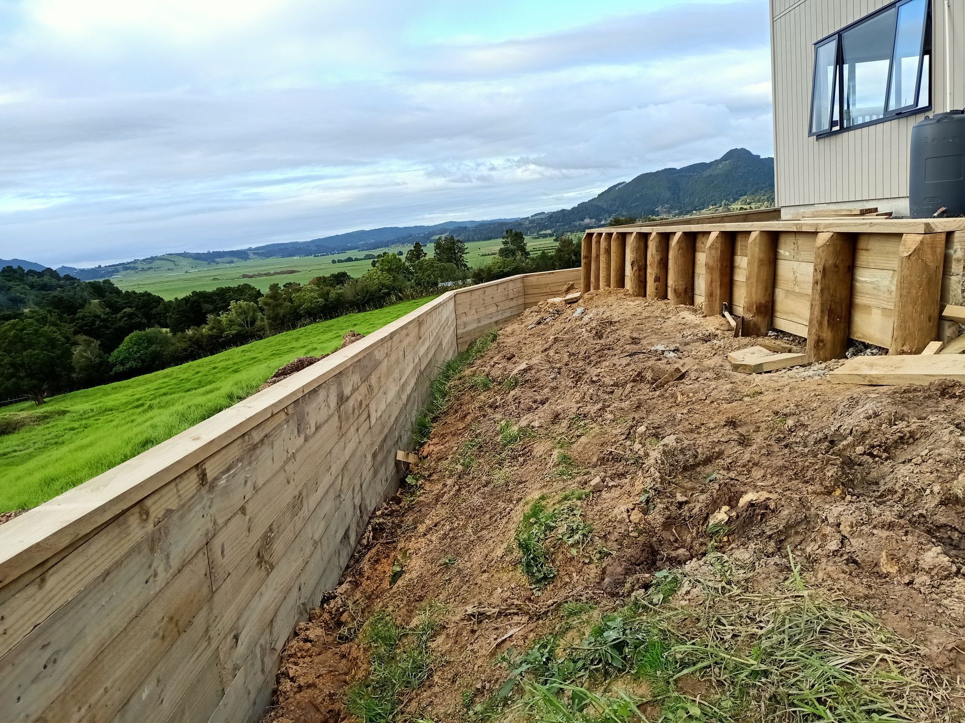 A wooden fence is sitting on top of a hill next to a house.