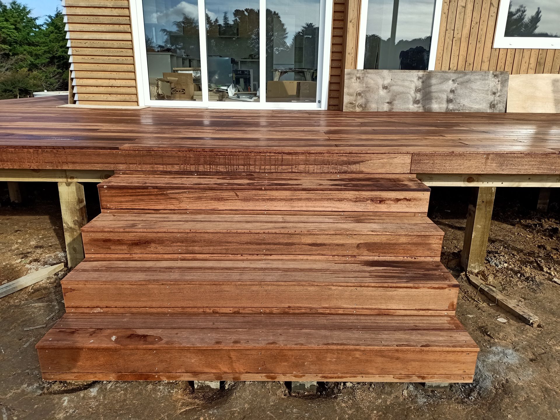 A wooden deck with stairs leading up to it in front of a house.