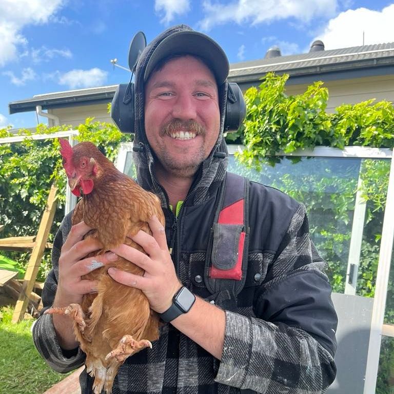 A man wearing headphones is holding a brown chicken