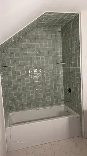 A bathroom with a bathtub and a shower with green tiles.