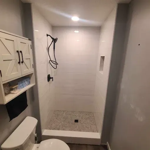 A bathroom with a toilet , shower , and cabinet.