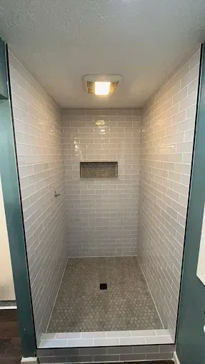 A shower stall with white tiles and a niche in the wall.
