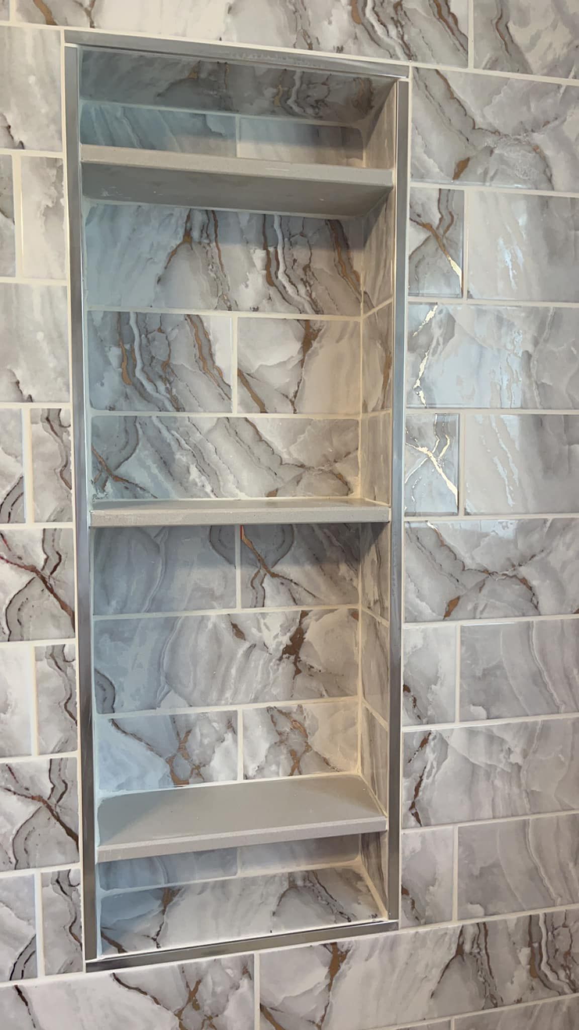 A bathroom with marble tiles and a shelf in the shower.