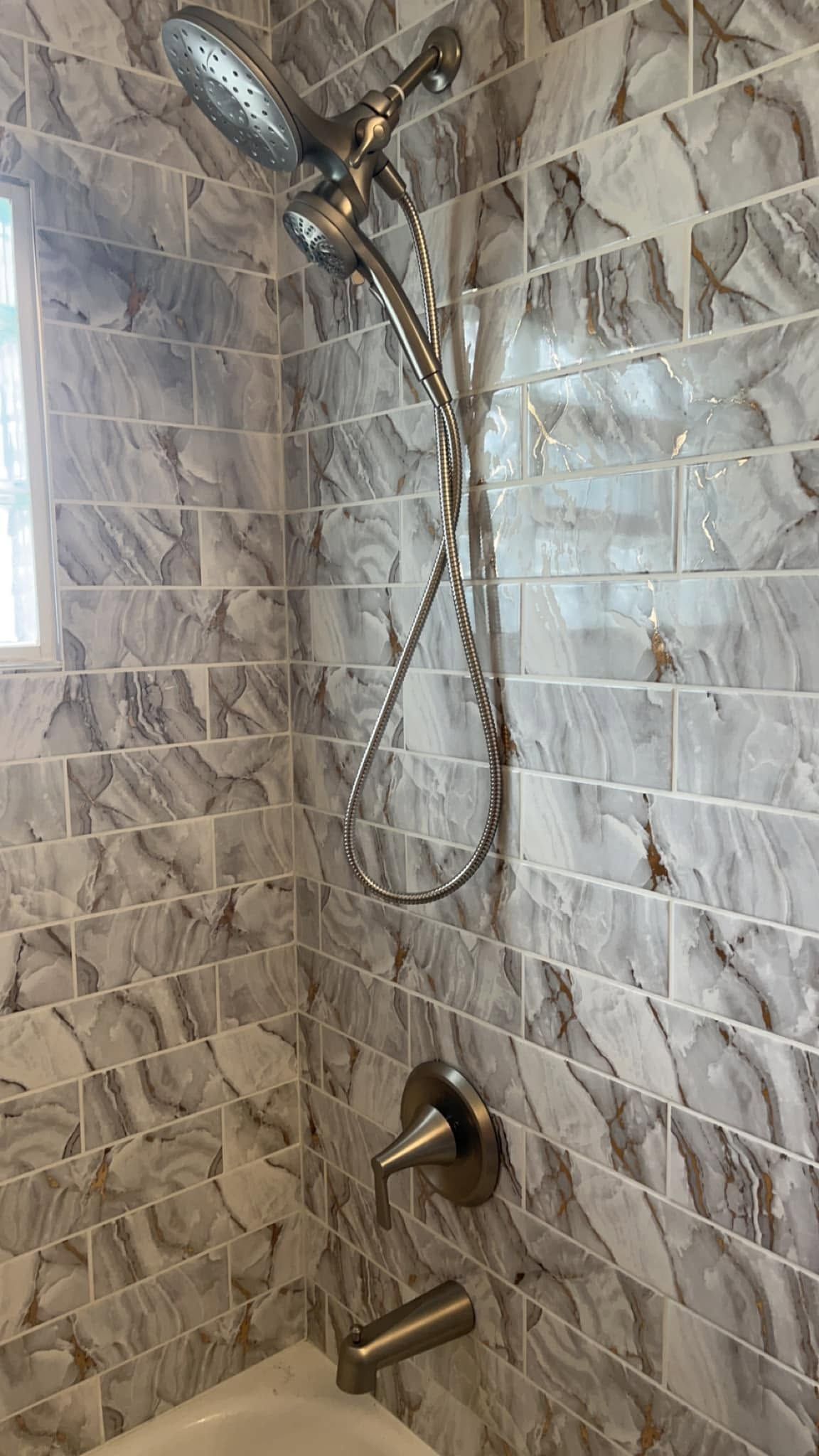 A bathroom with marble tiles and a shower head.