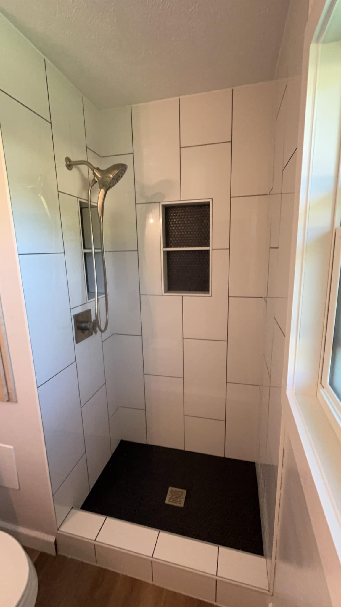 A bathroom with a shower , toilet and window.