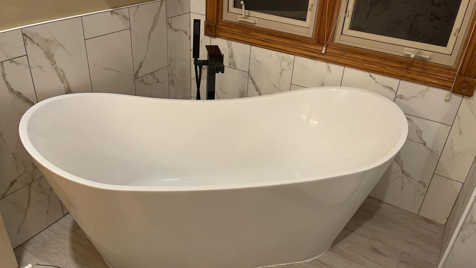 A white bathtub is sitting in a bathroom next to a window.