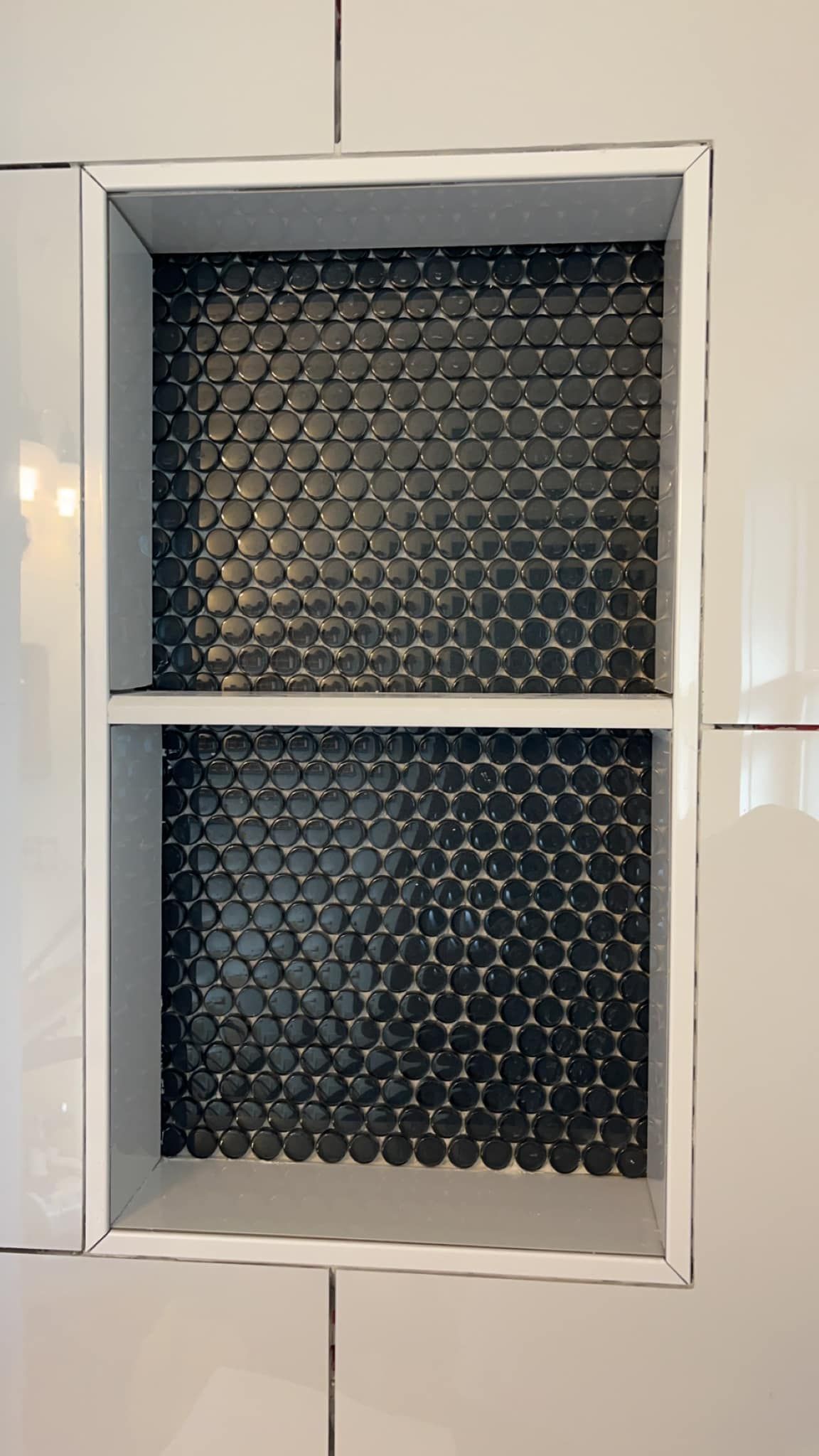 A bathroom shelf with black and white tiles on the wall.