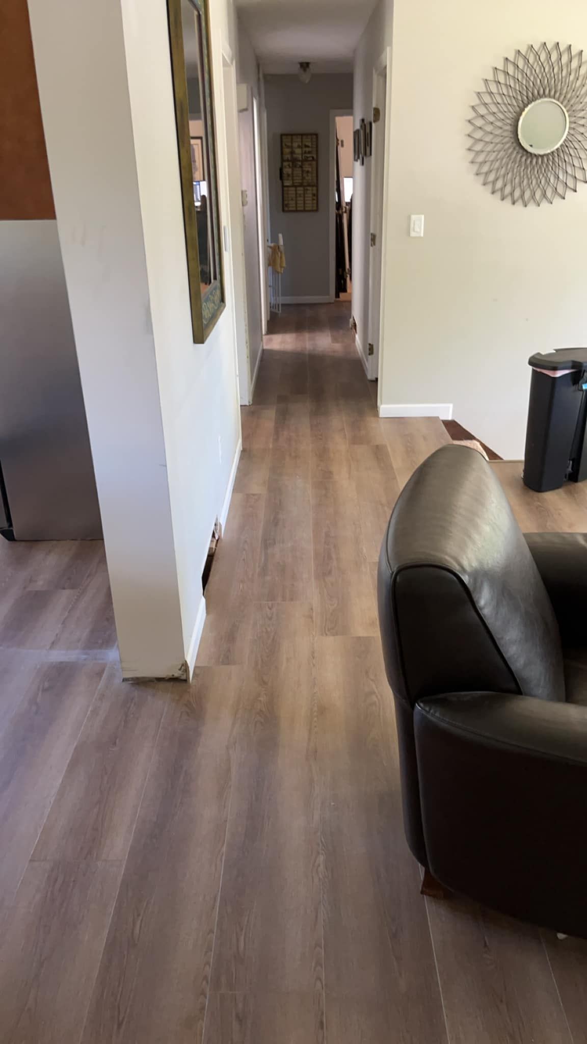 A long hallway in a living room with hardwood floors and a chair.