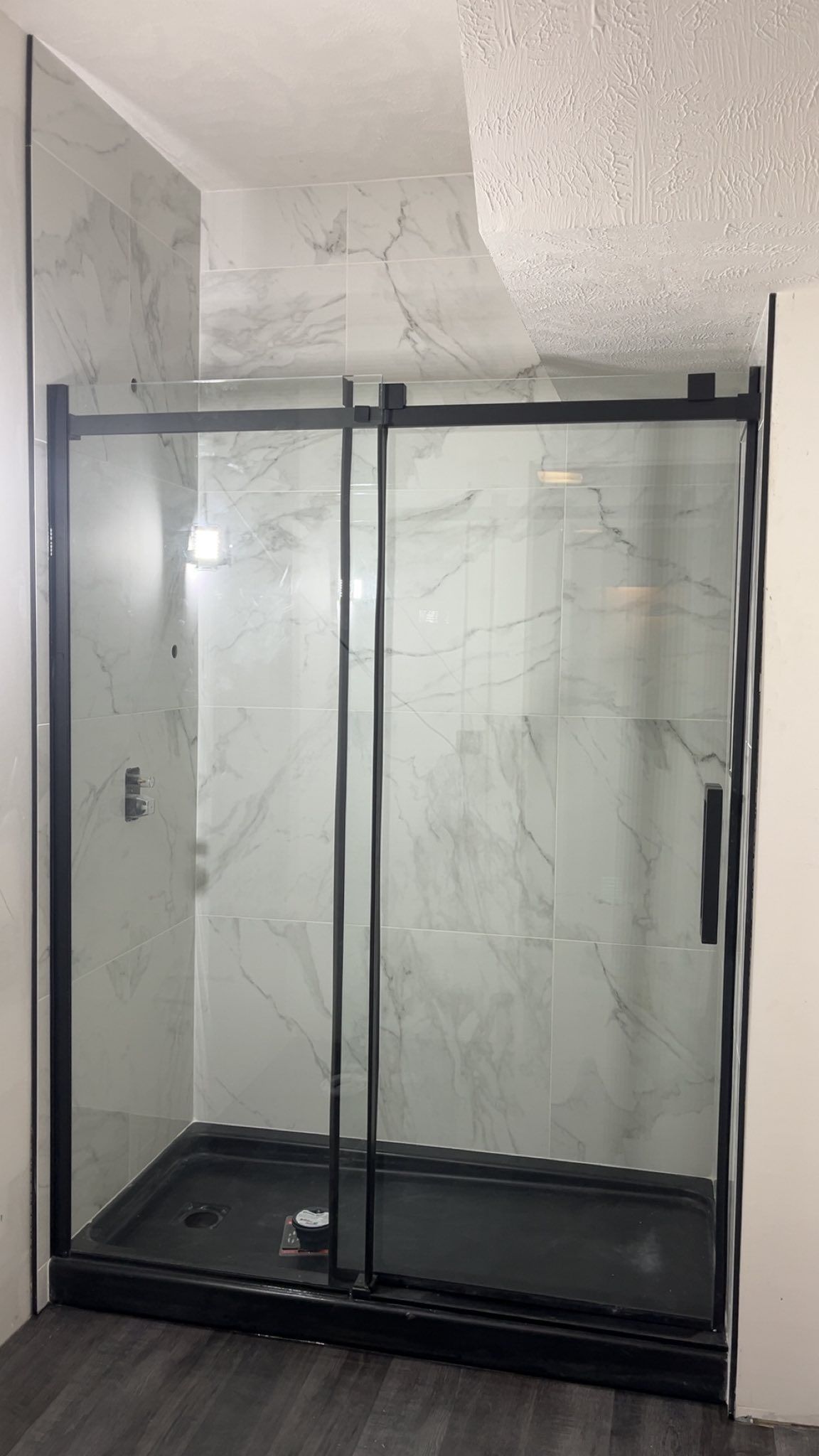 A shower stall with a black frame and sliding glass doors in a bathroom.
