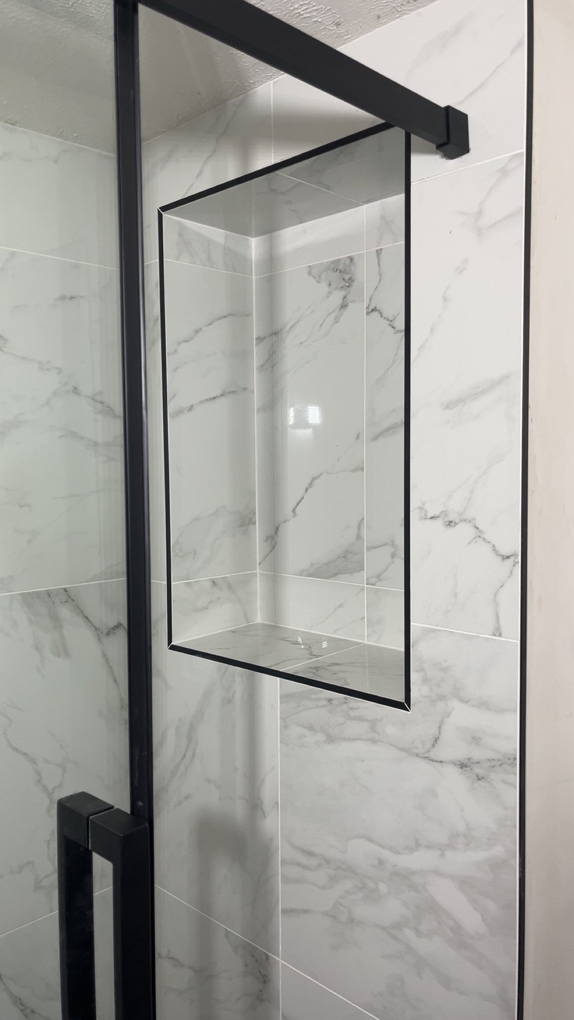 A shower stall with a black frame and a marble wall.